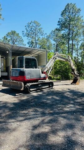 a red and white excavator is parked in a parking lot . — Naples, FL — Affordable Pros Removal Services LLC