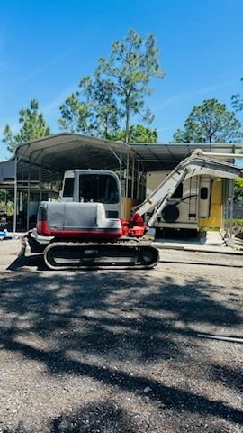 a small excavator is parked in front of a house under a canopy . — Naples, FL — Affordable Pros Removal Services LLC