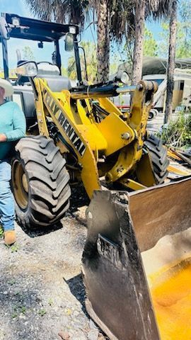a man is standing next to a yellow bulldozer . — Naples, FL — Affordable Pros Removal Services LLC