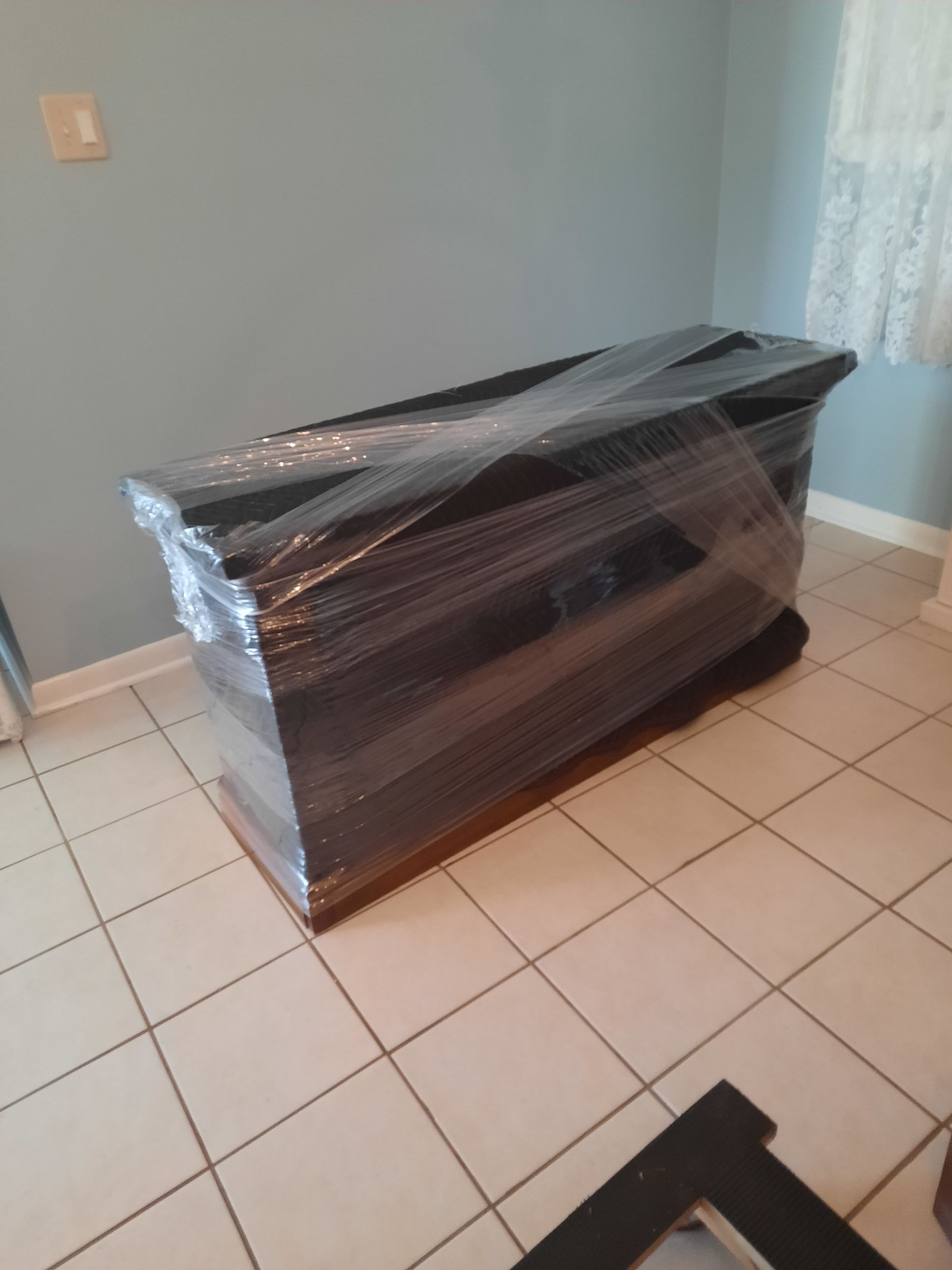 A black box wrapped in plastic is sitting on a tiled floor in a room.