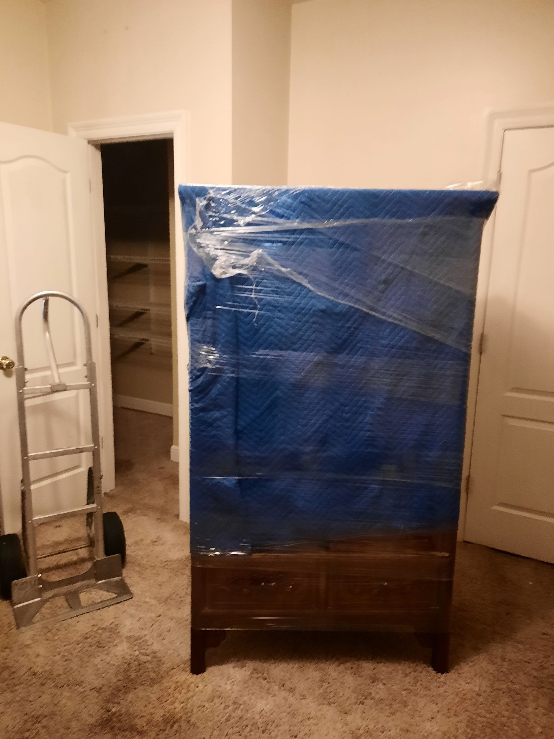 A dresser is wrapped in blue plastic in a room.