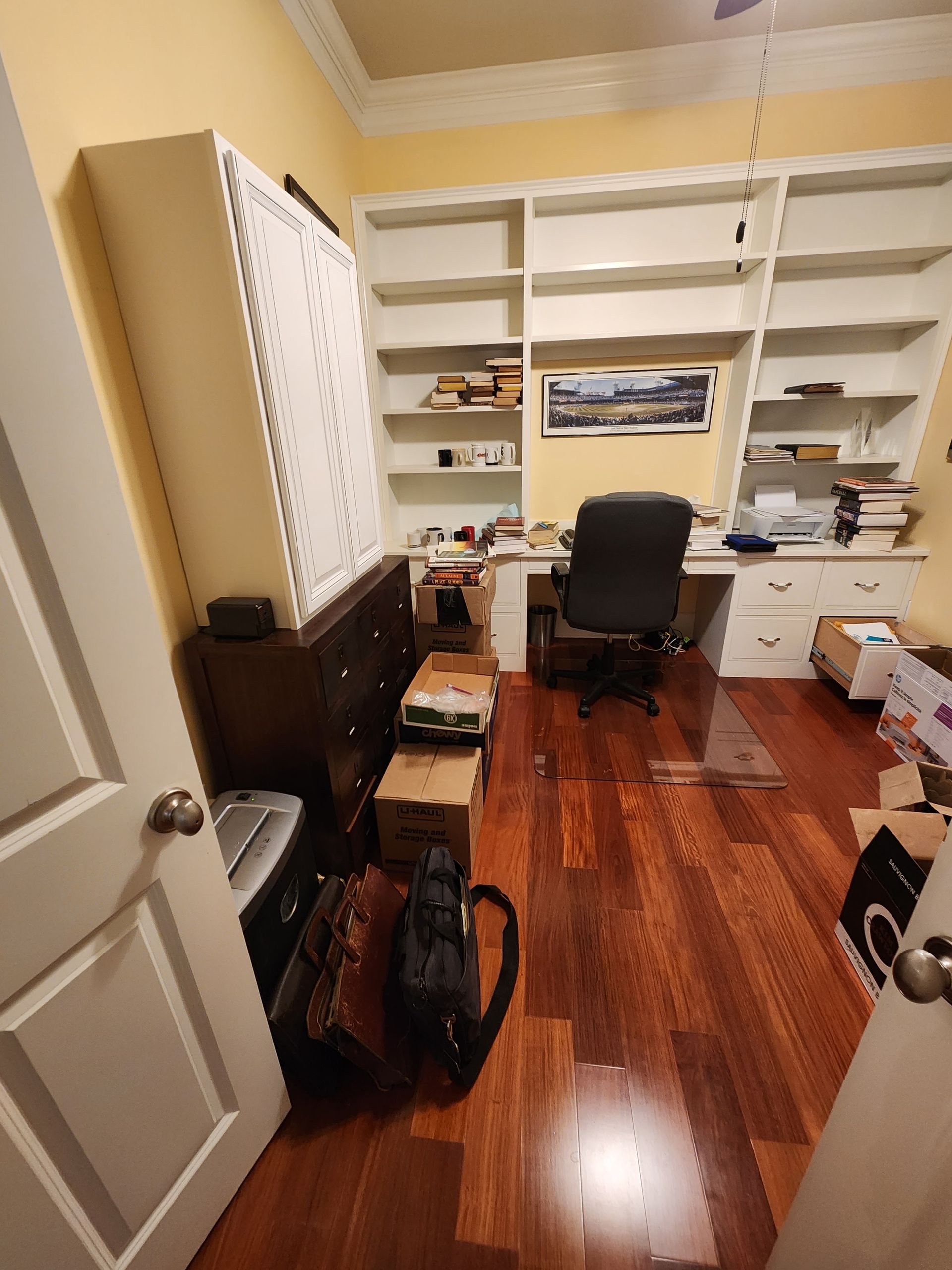 A room with hardwood floors , a desk , shelves and a chair.