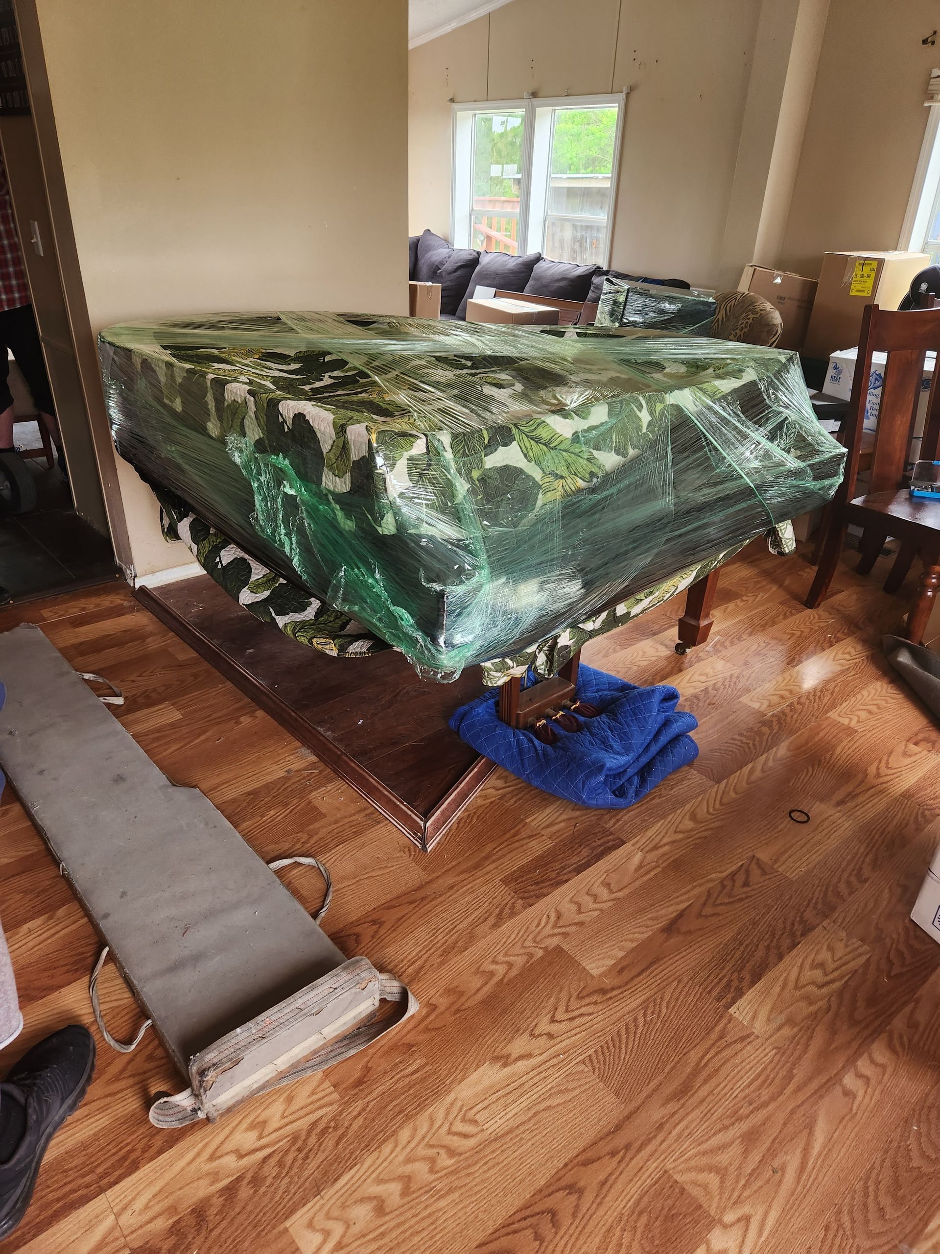 A piano is wrapped in plastic and sitting on a wooden floor in a living room.