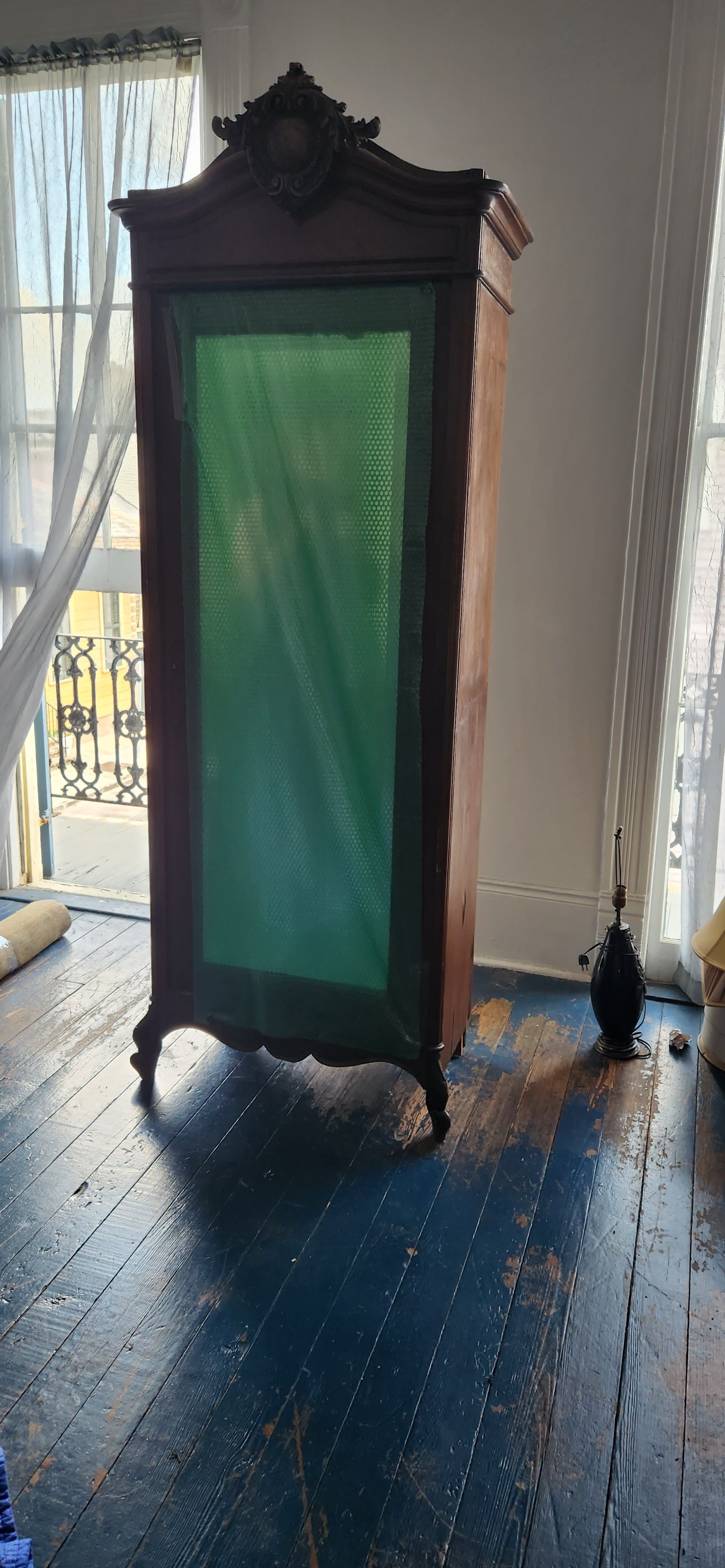 An antique wardrobe with a green curtain is sitting in a room next to a window.