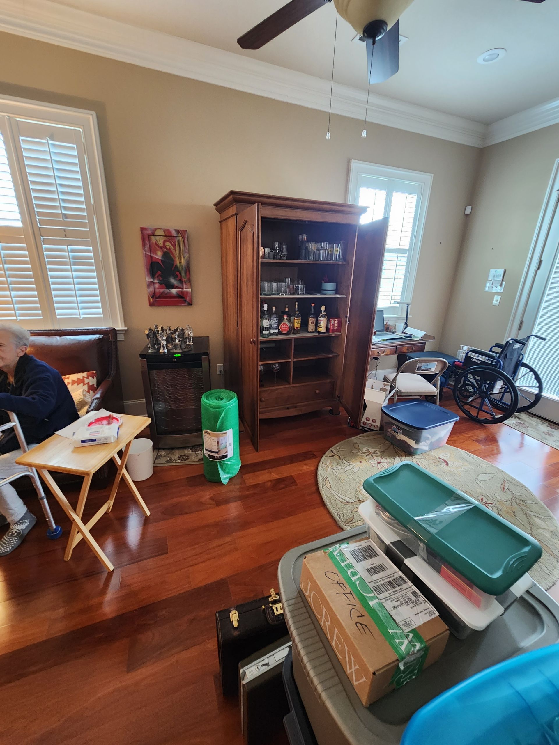 A man is sitting at a table in a living room with a ceiling fan.