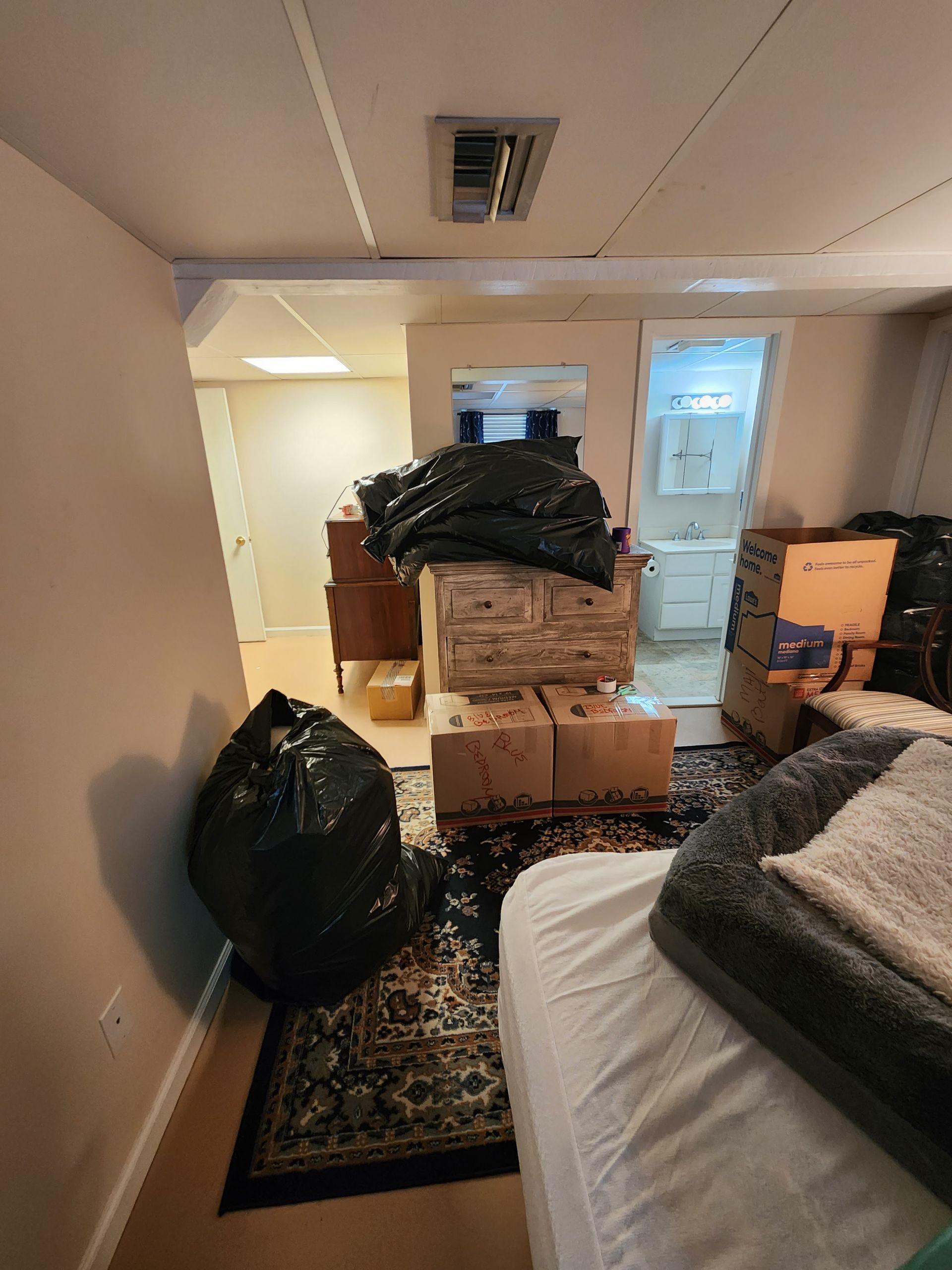 A bedroom filled with boxes and bags and a bed.