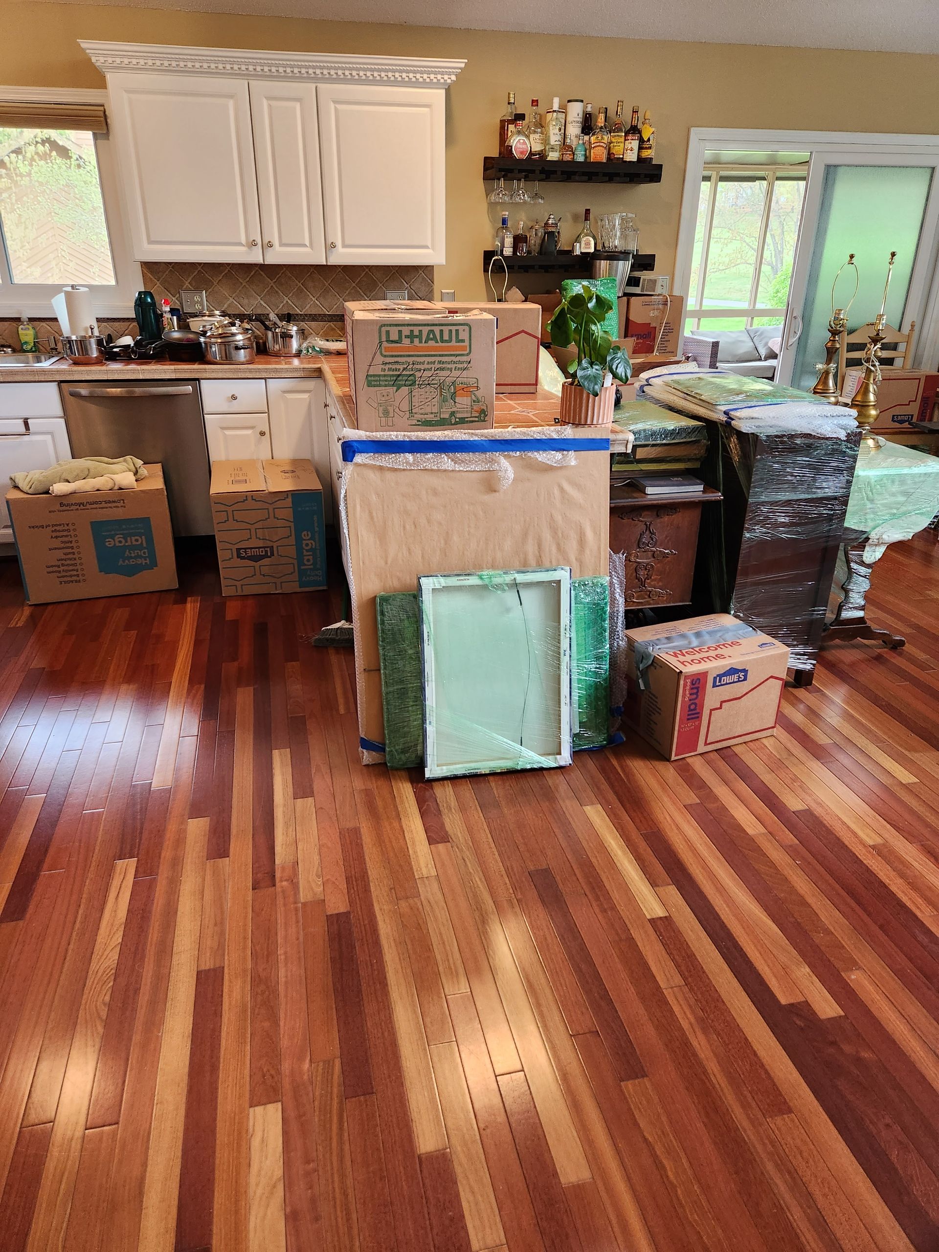 A kitchen with wooden floors and boxes on the floor.