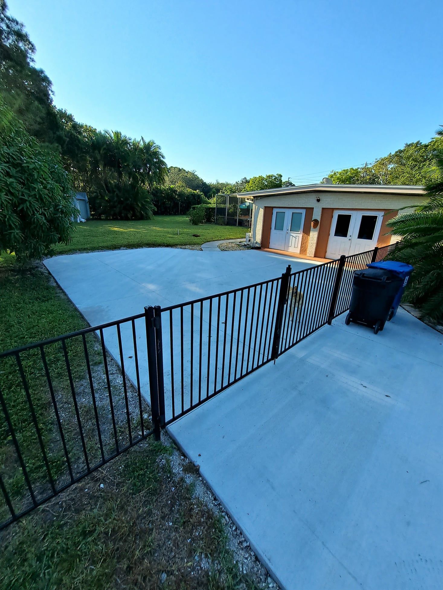 A fence surrounds a concrete driveway in front of a house.