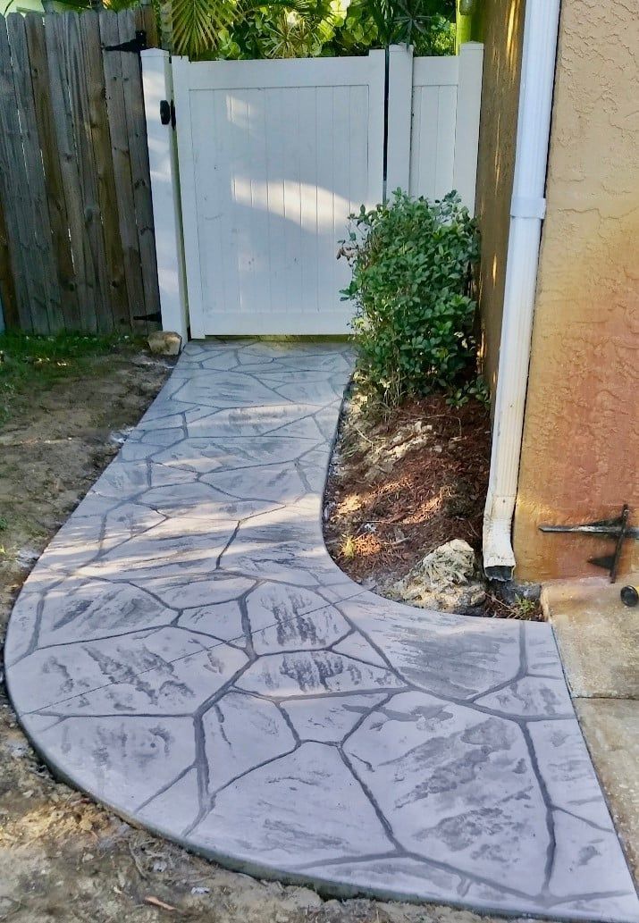 A concrete walkway leading to a white gate in a backyard.