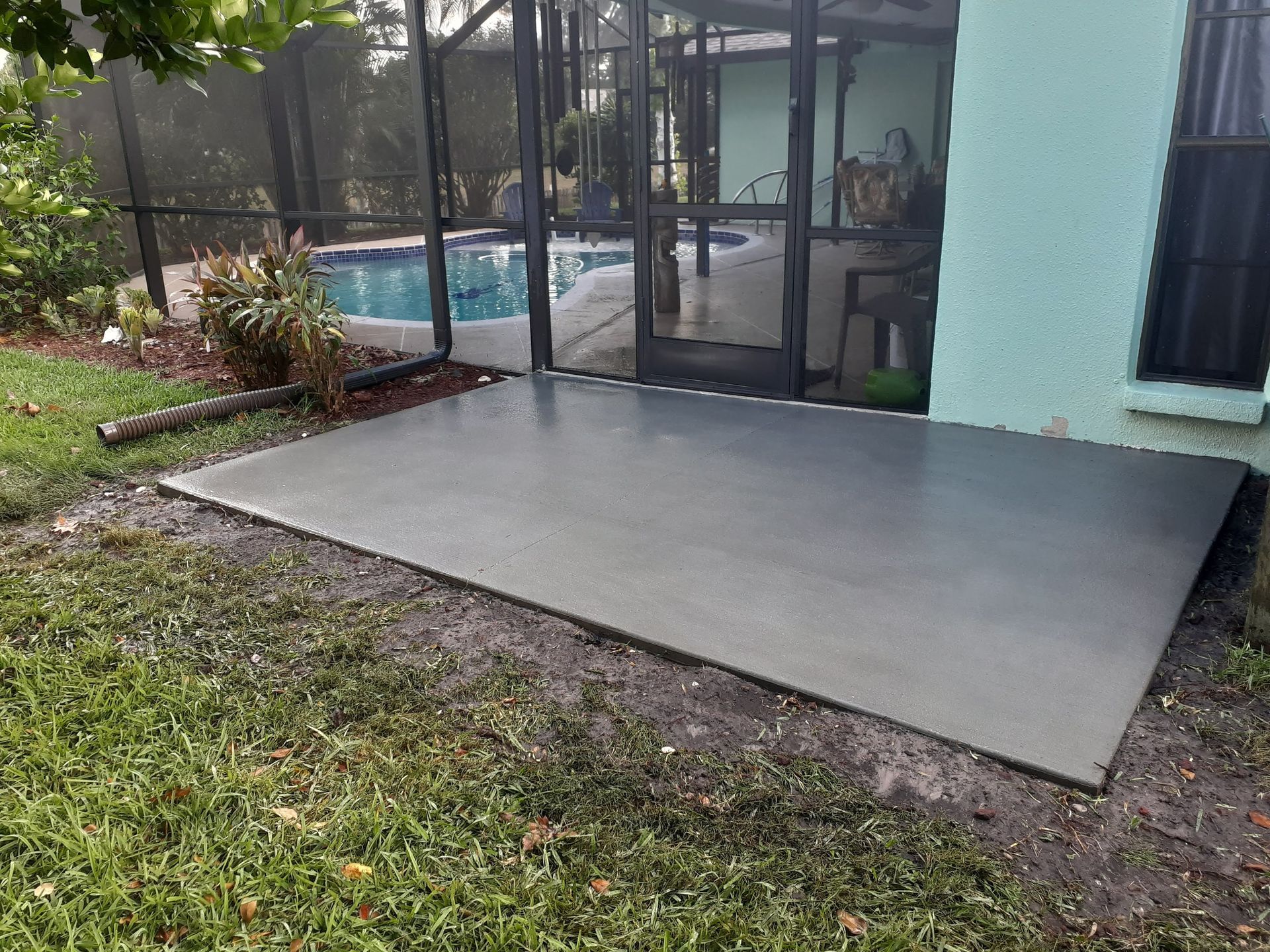 A concrete patio with a screened in pool in the background.