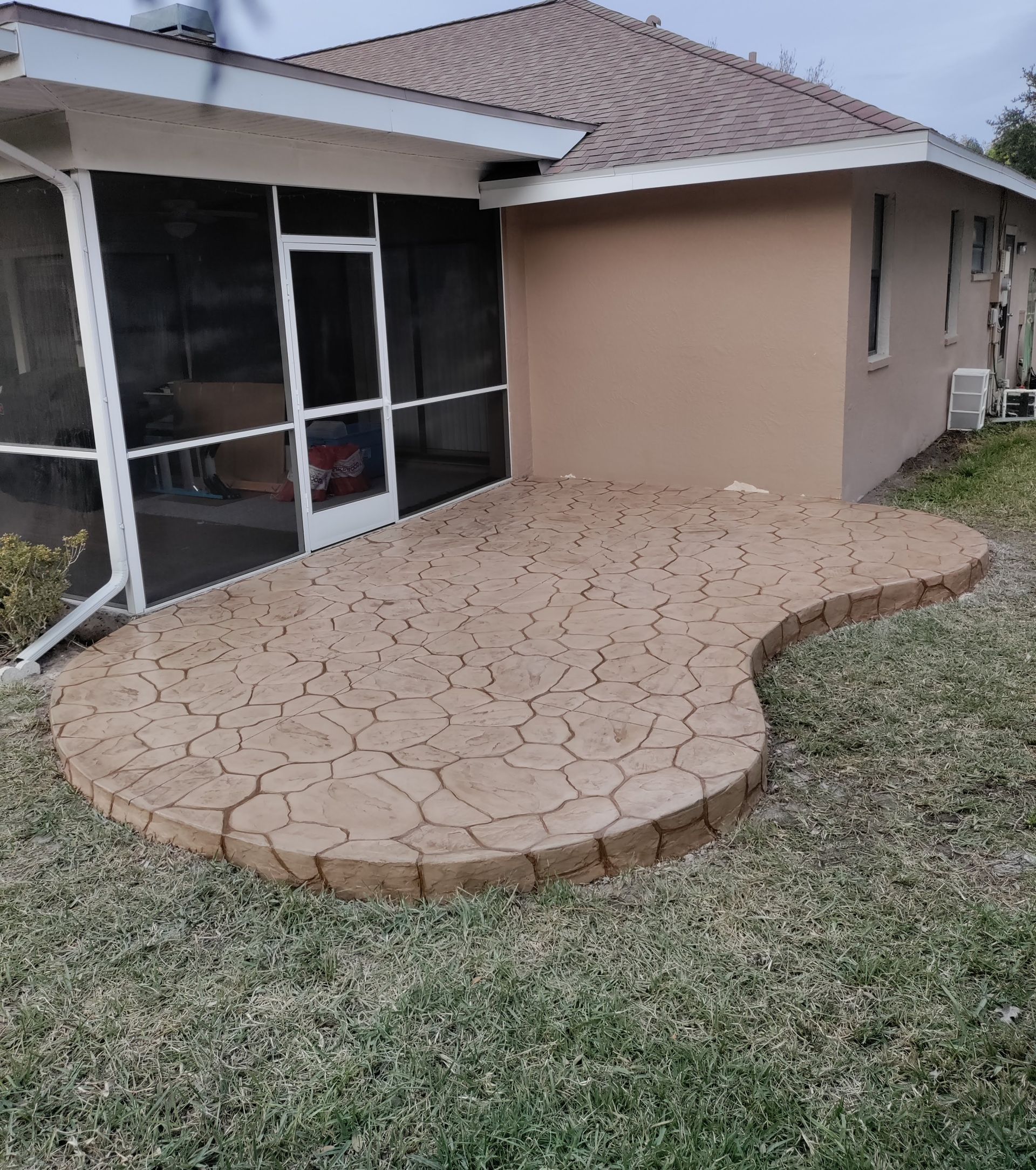 A house with a screened in porch and a patio in front of it.