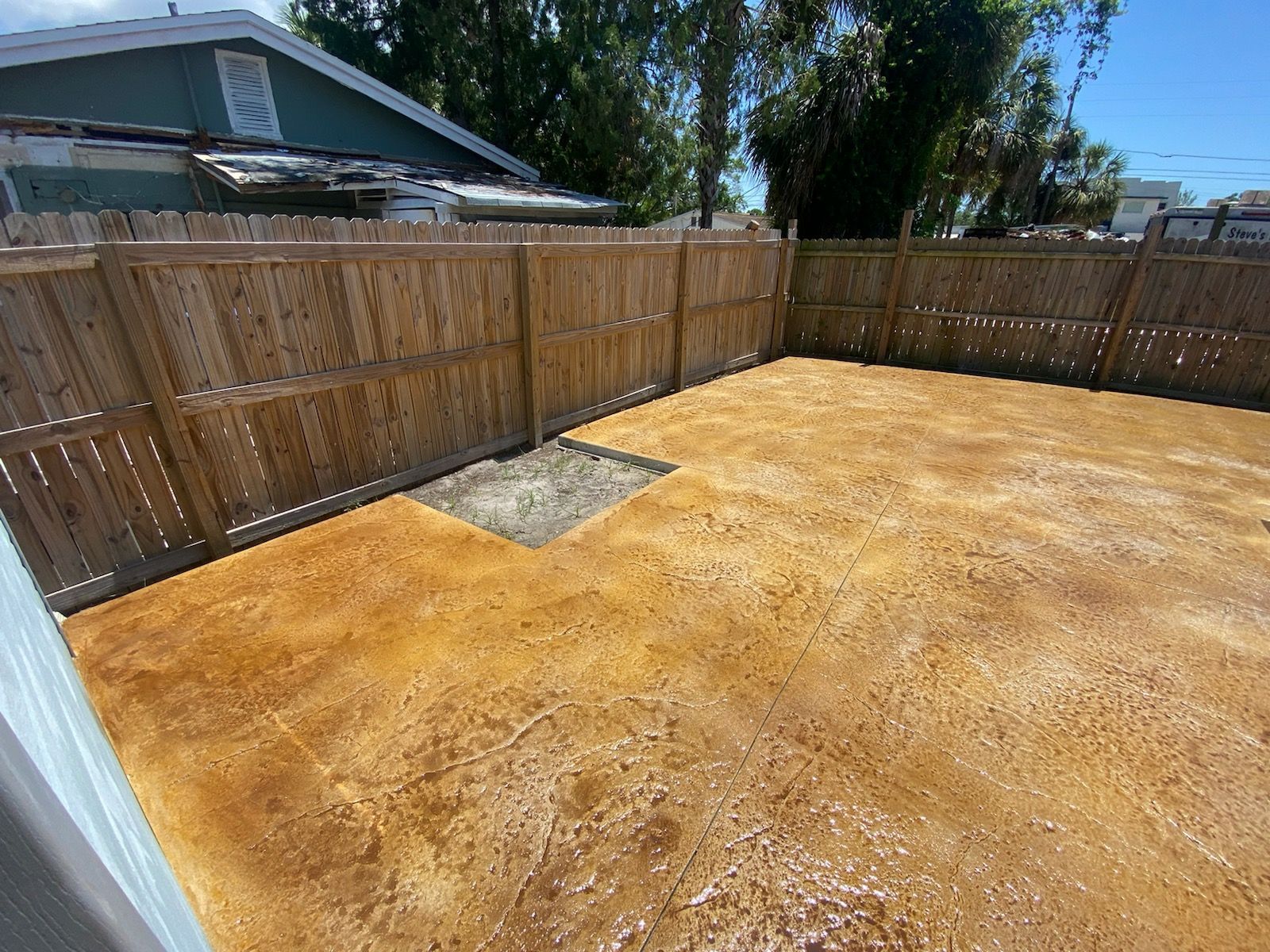 A backyard with a wooden fence and a concrete floor.