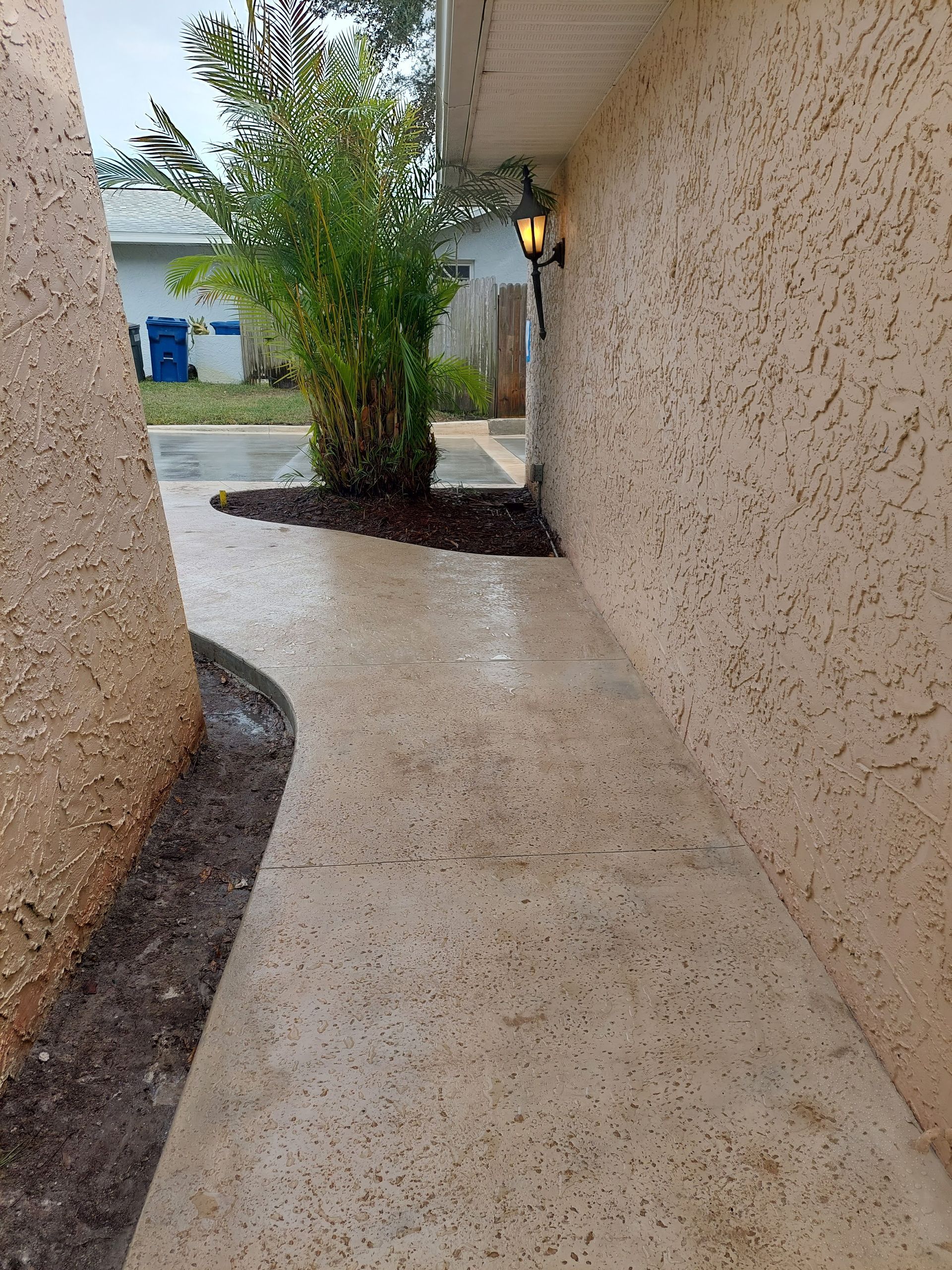 A sidewalk leading to a house with a lamp on the wall.
