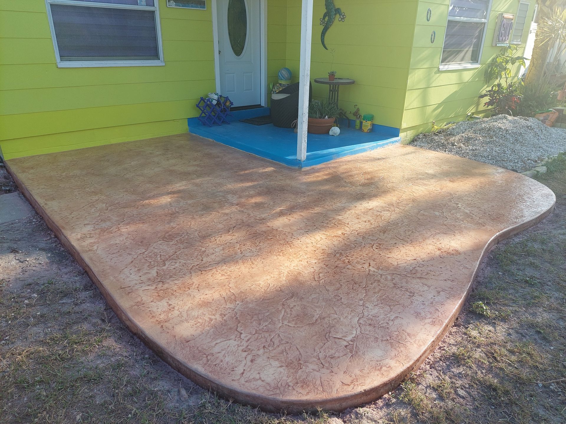 A yellow house with a blue porch and a concrete patio in front of it.