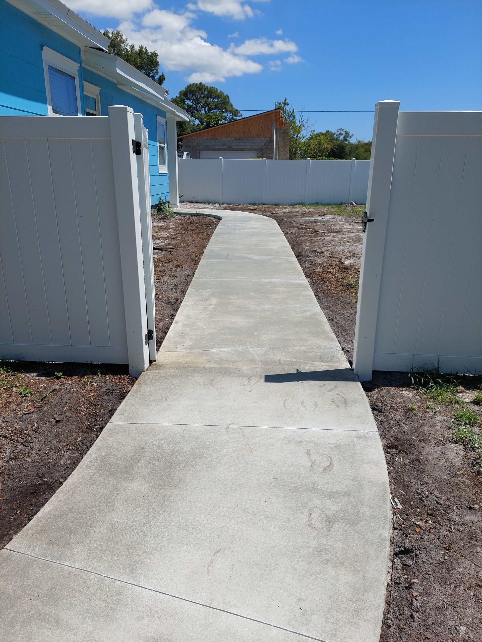 A concrete walkway leading to a white fence