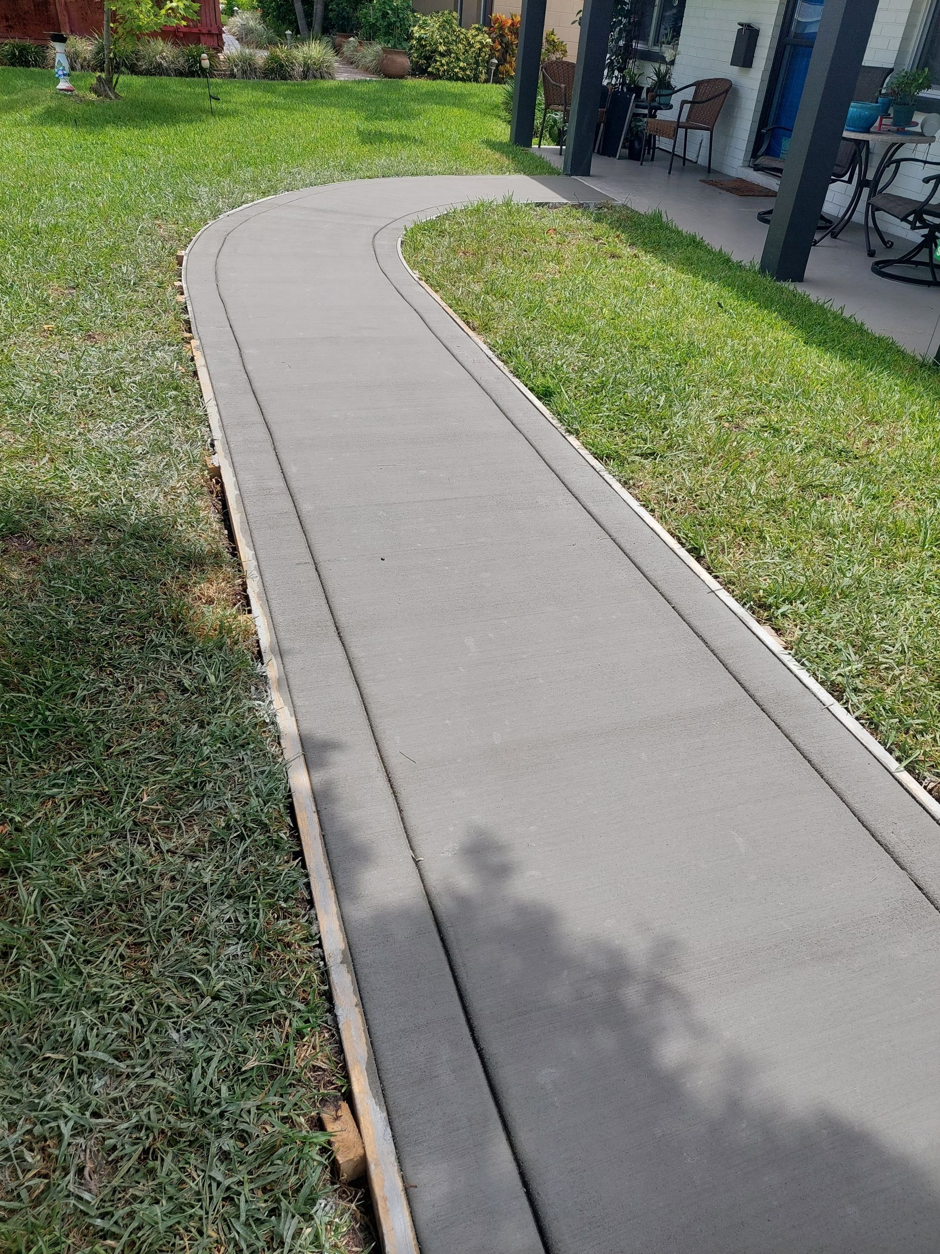A concrete walkway going through a lush green yard.