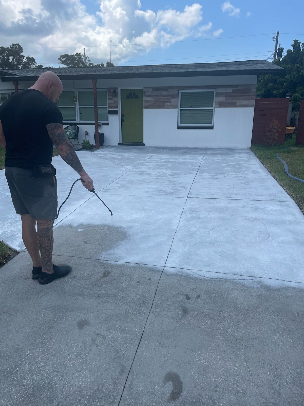 A man is spraying white paint on a driveway in front of a house.