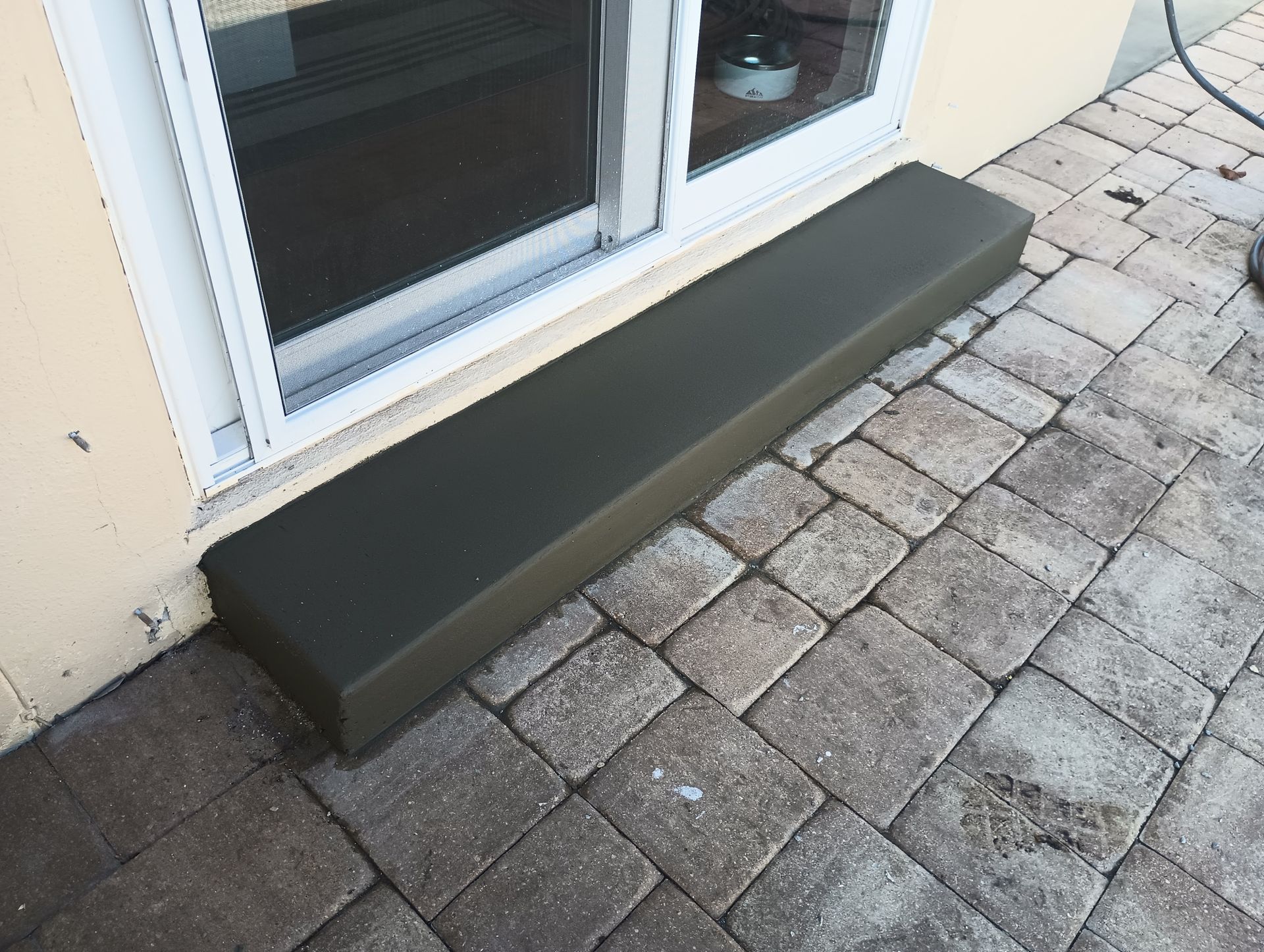 A concrete step sits on a brick sidewalk next to a sliding glass door