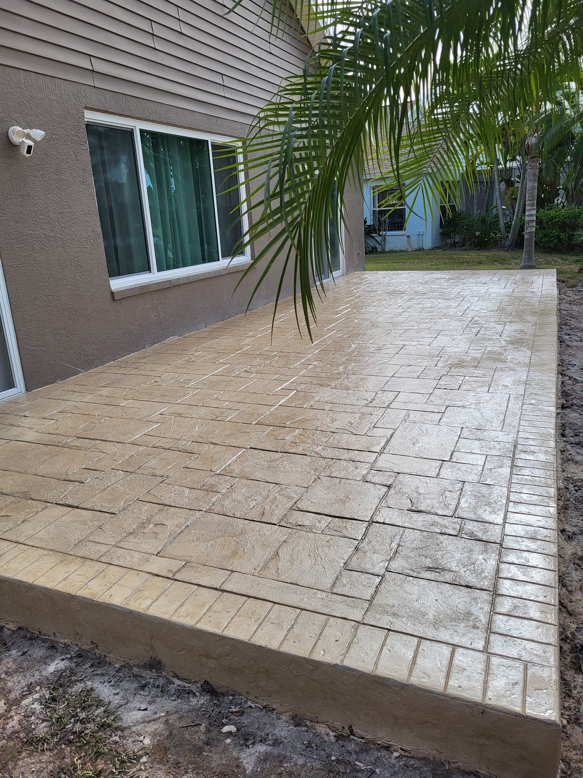 A concrete patio in front of a house with a palm tree in the background.