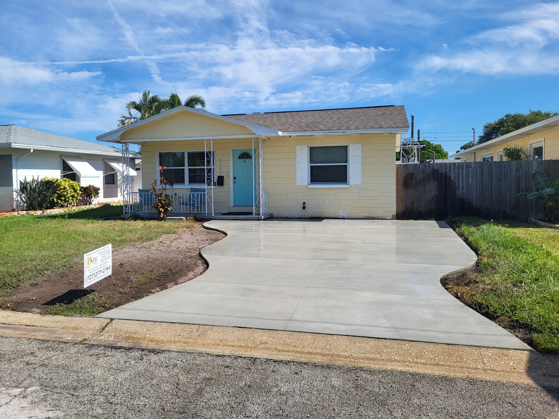 A yellow house with a blue door and a concrete driveway in front of it.