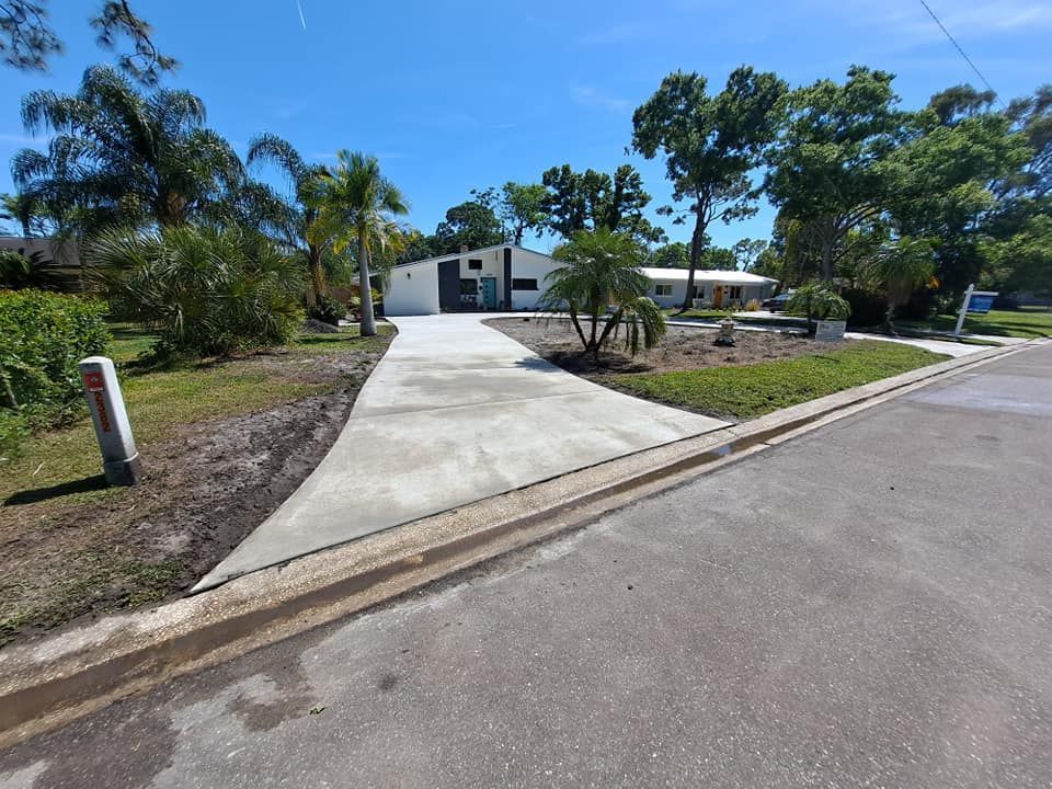 A concrete driveway leading to a house with palm trees in the background.