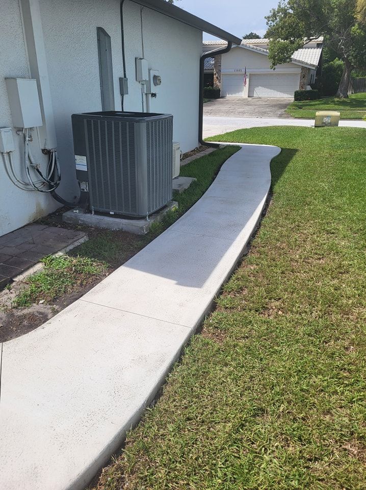 A concrete walkway leading to a house with an air conditioner on the side of it.