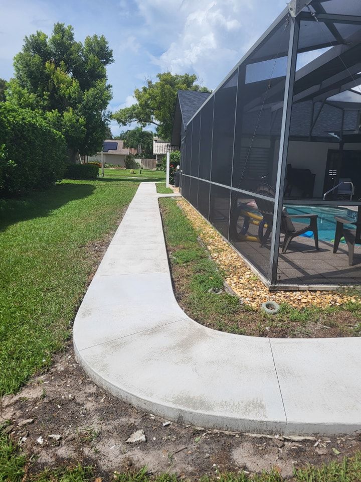 A concrete walkway leading to a screened in pool area.