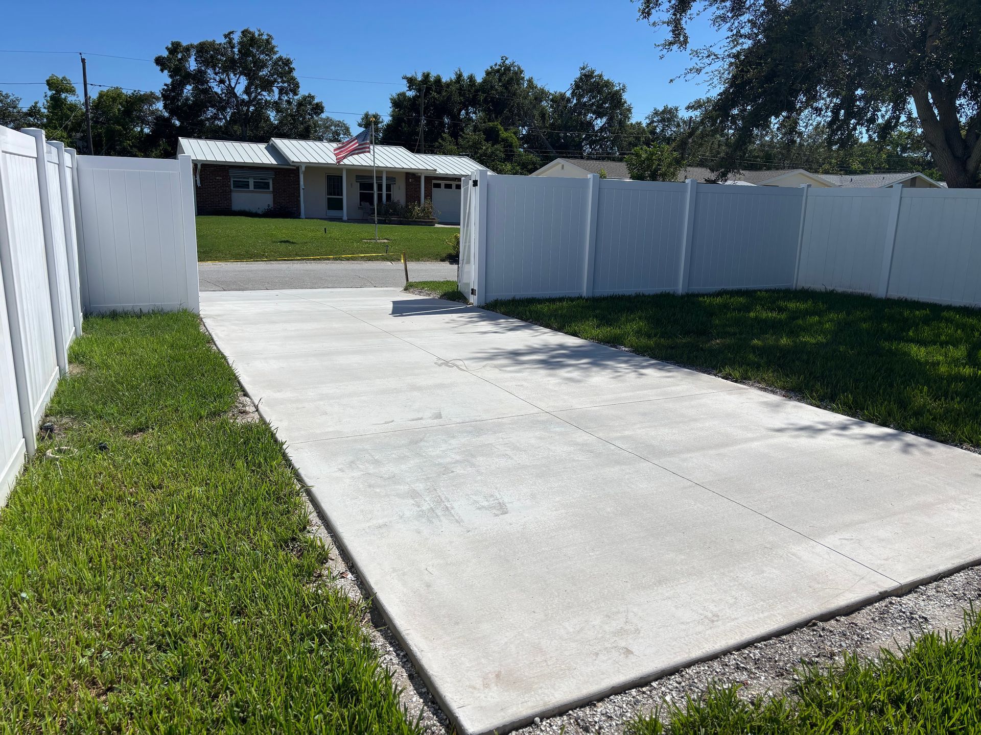 A concrete driveway leading to a house with a white fence