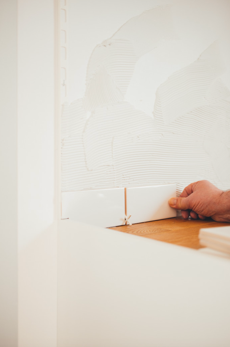A person is laying tiles on a wooden floor.