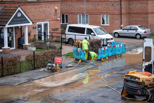 A group of people are working on a flooded street in front of a building.
