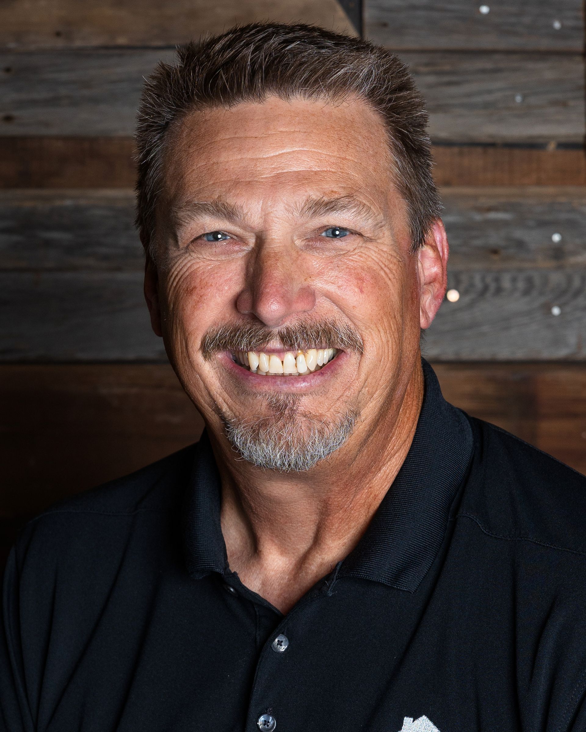 A man in a grey shirt is smiling for the camera.