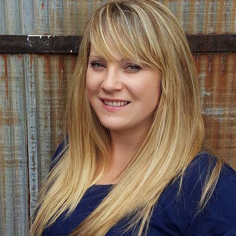 A woman with long blonde hair and a blue shirt smiles for the camera