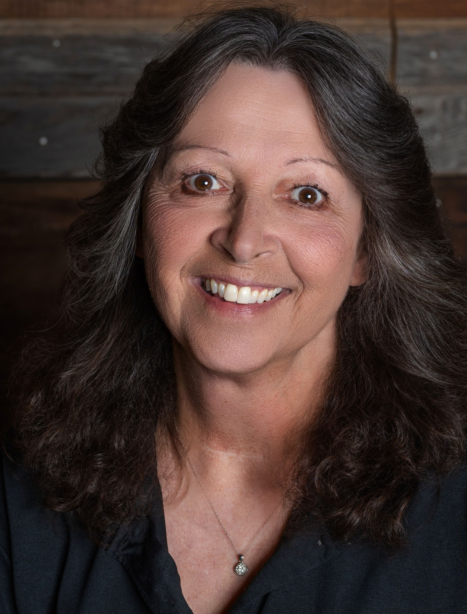 A woman in a white shirt is smiling and leaning against a wall.