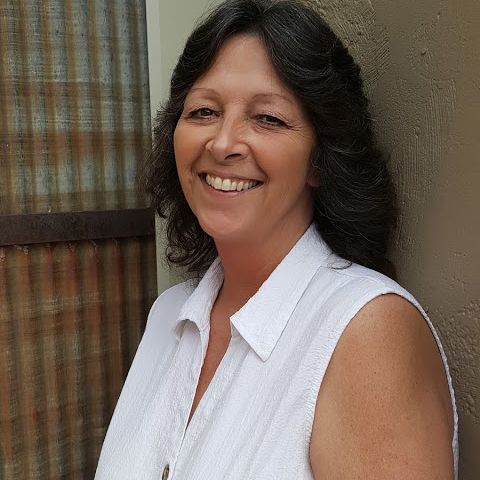 A woman in a white shirt is smiling and leaning against a wall.