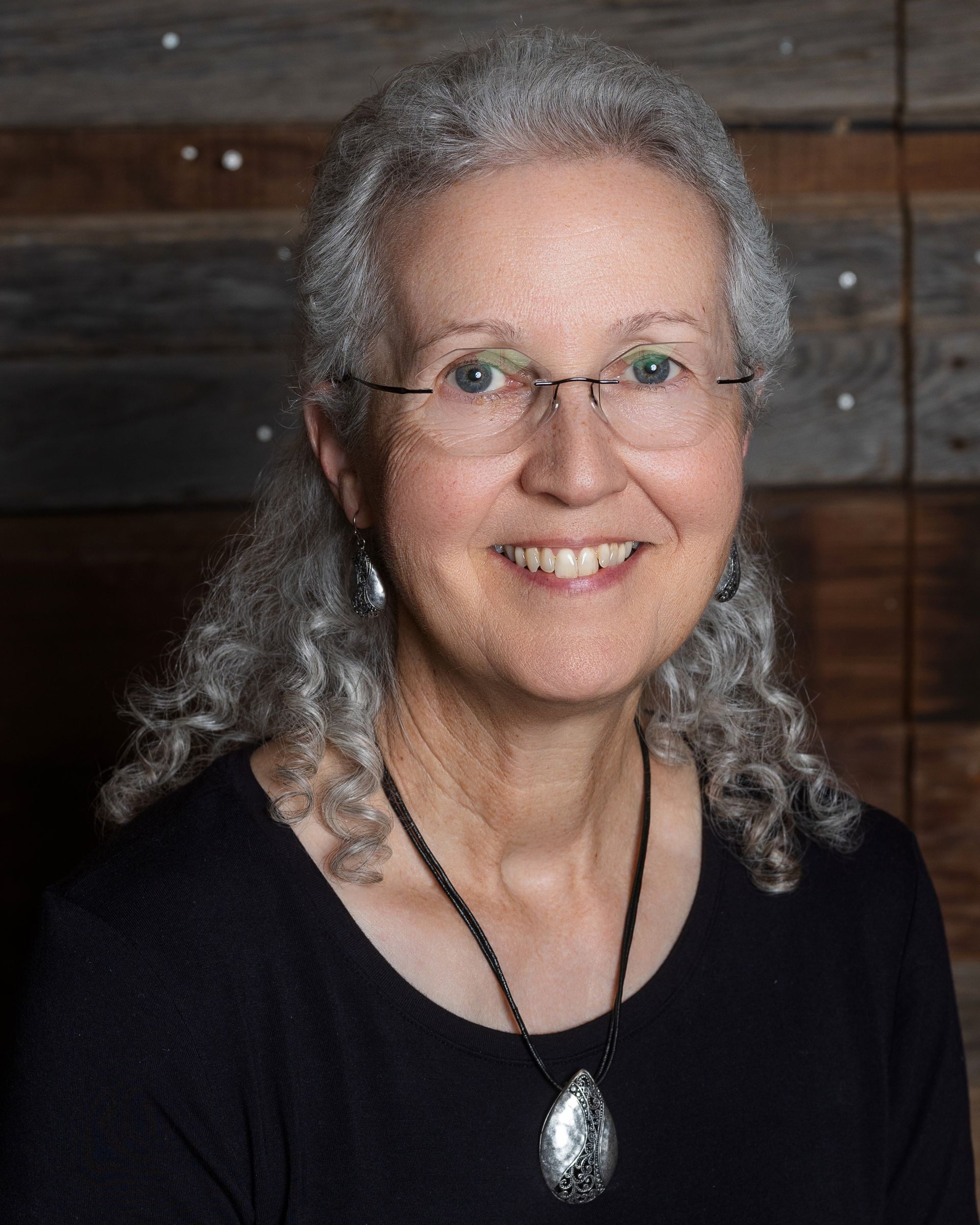 A woman wearing glasses and a plaid shirt is standing in front of a wooden wall.