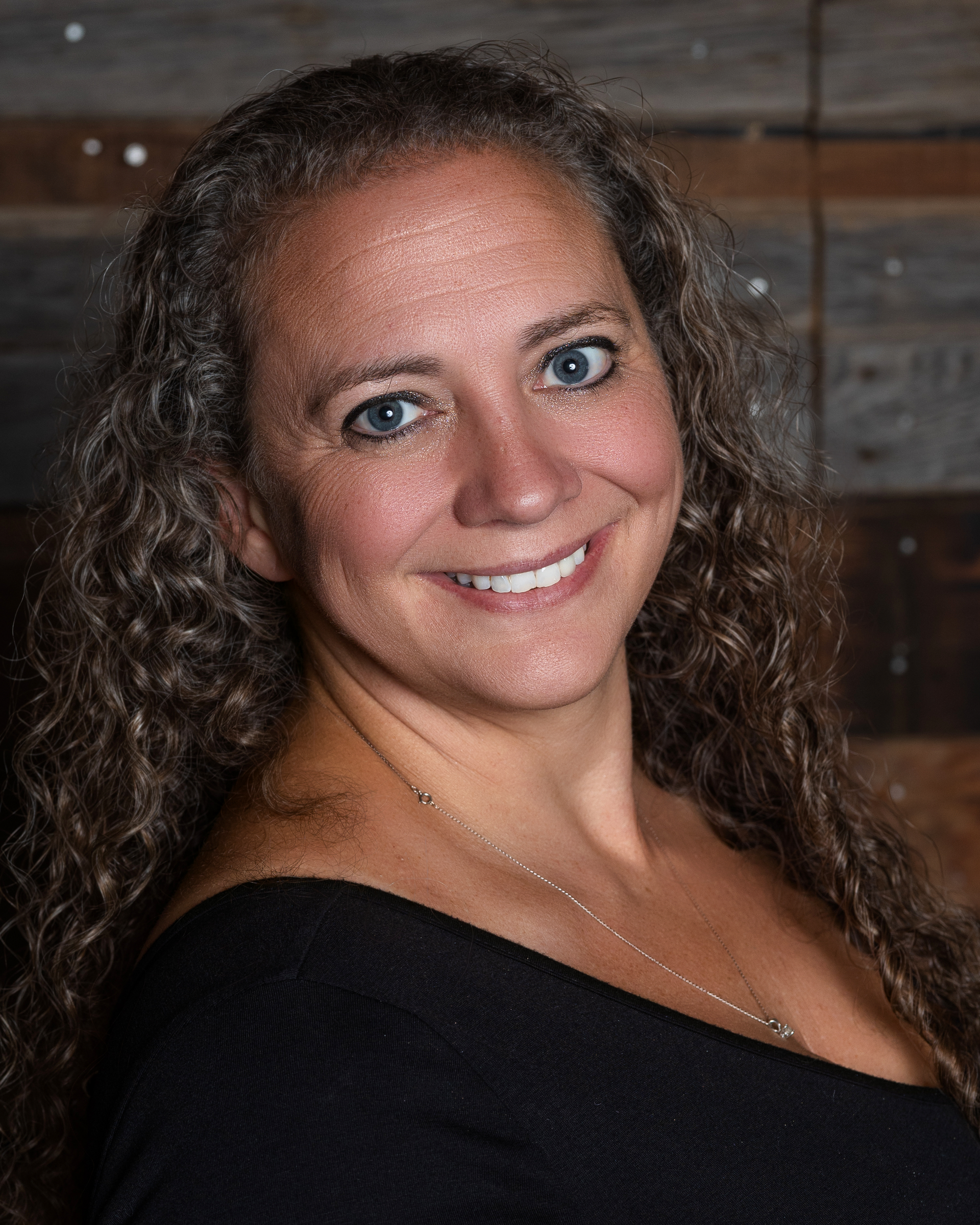 A woman with curly hair is wearing a blue shirt and smiling.