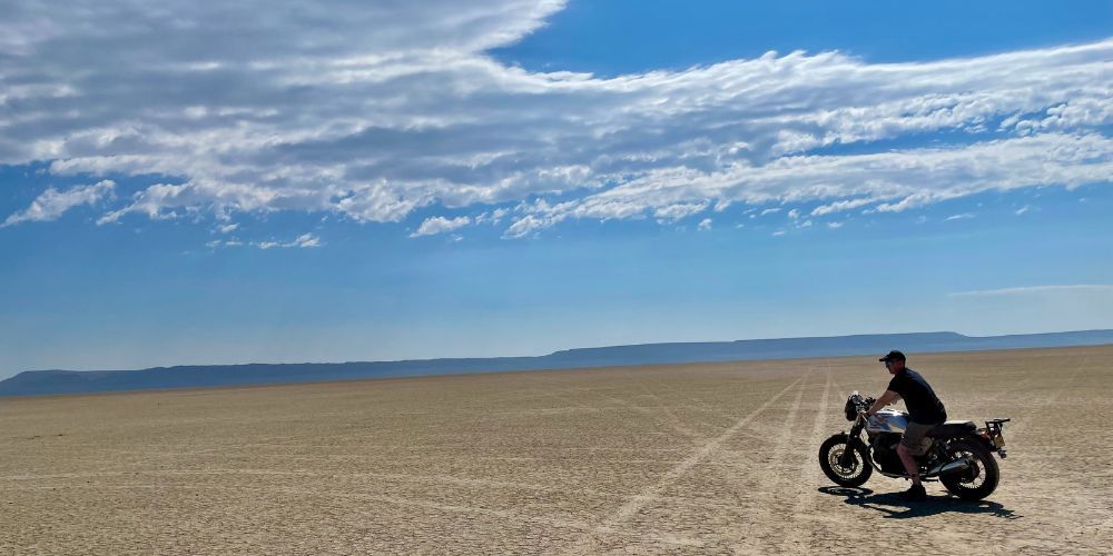 A man is riding a motorcycle in the middle of a desert.