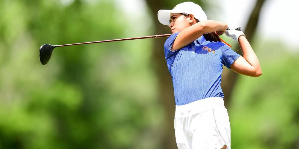 A woman is swinging a golf club on a golf course.