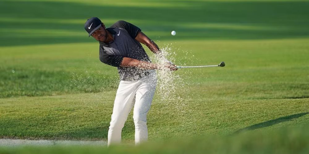 A man is hitting a golf ball out of a bunker on a golf course.