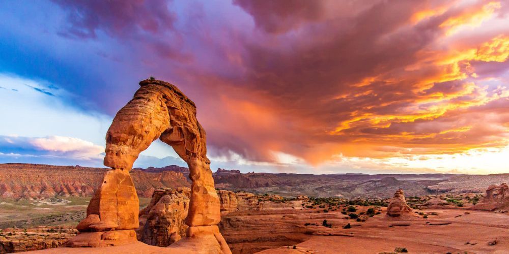 A large rock formation in the middle of a desert with a sunset in the background.