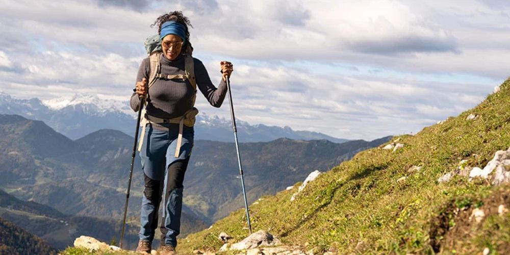 A woman is hiking up a mountain with a backpack and walking poles.