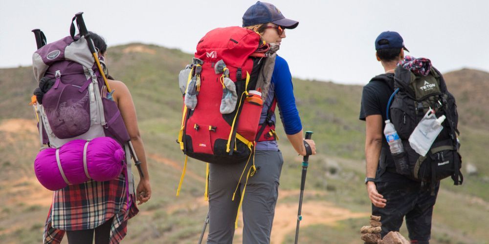 A group of people with backpacks are walking down a dirt road.