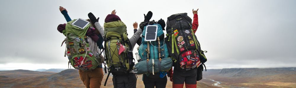 A group of people with backpacks standing next to each other on top of a hill.