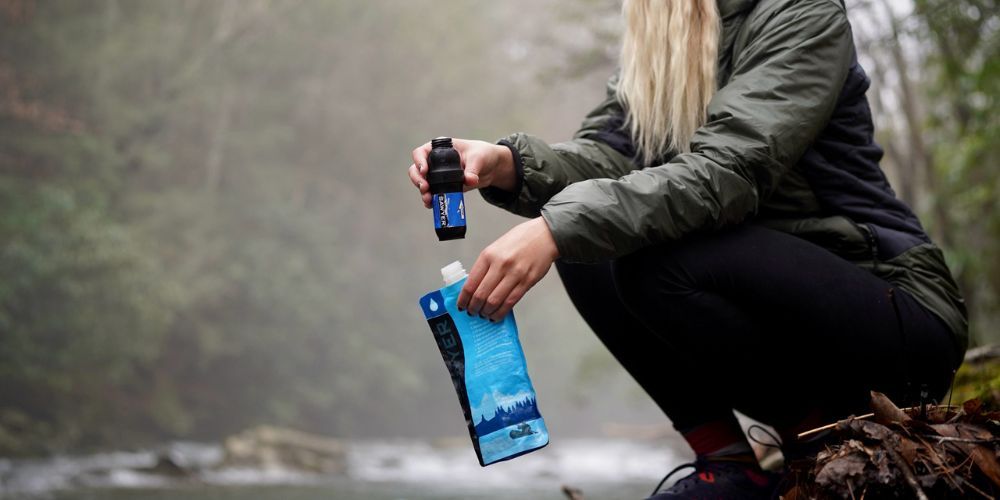 woman at a creek filling up her water filtration pouch