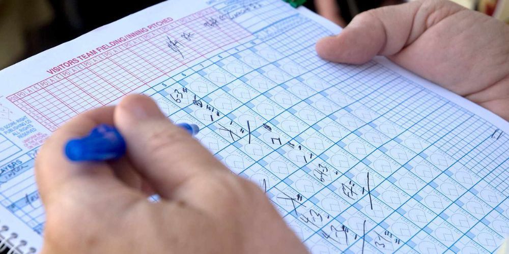 person writing in a baseball scorebook