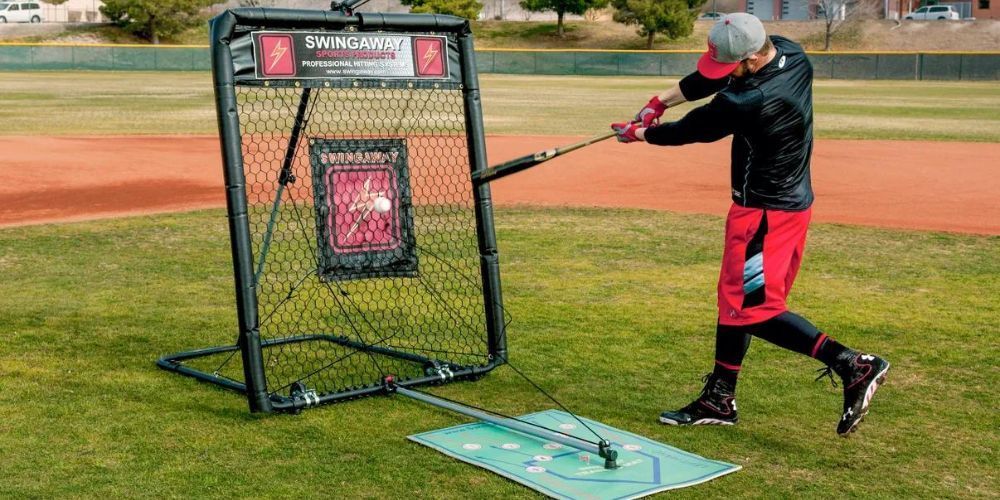 A man is swinging a bat at a target on a baseball field.