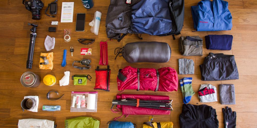 A wooden table topped with a bunch of clothes and a backpack.