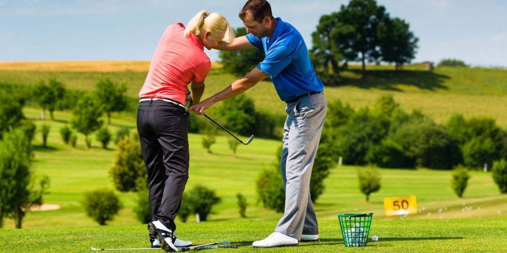 A man is helping a woman swing a golf club on a golf course.