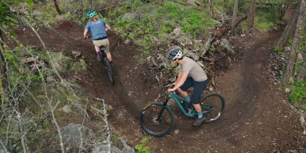 A man and a woman are riding bikes on a trail in the woods.