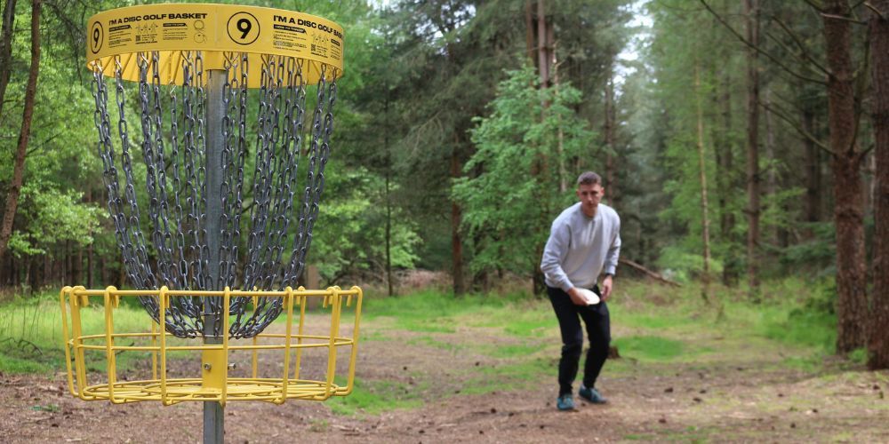 A man is throwing a frisbee at a frisbee golf course in the woods.